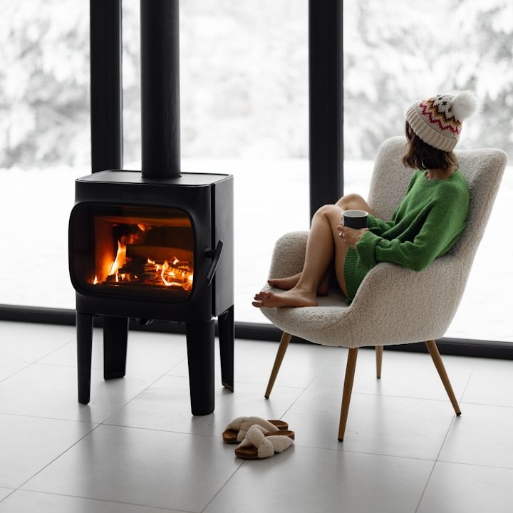 Person in einem grünen Kleid sitzt entspannt in einem Sessel neben einem Kamin.